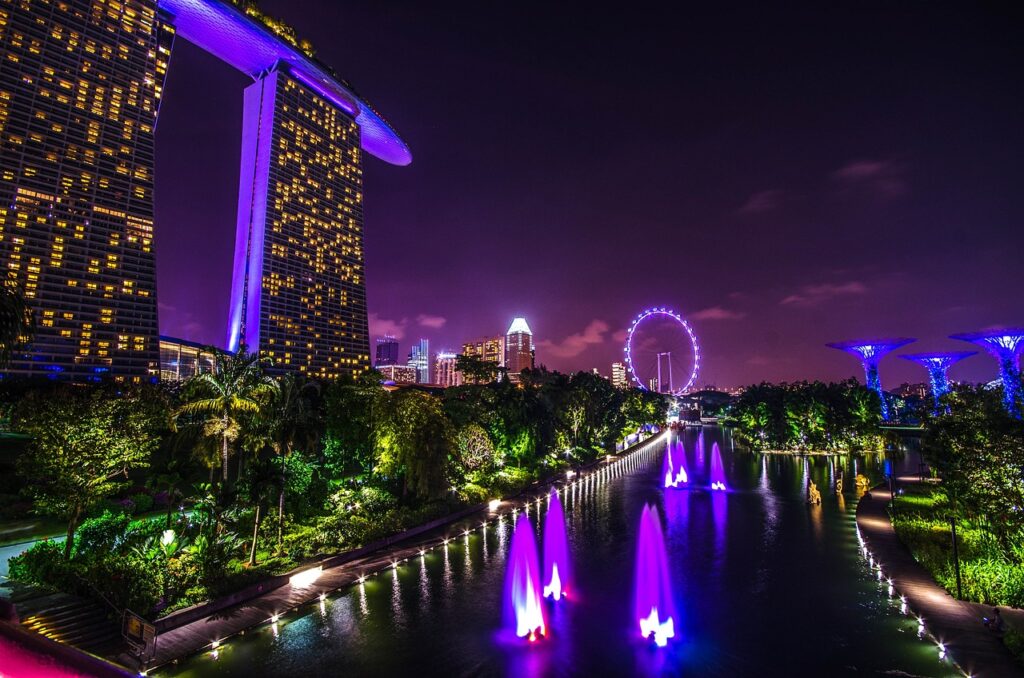 Aerial view of Marina Bay, Singapore skyline with Marina Bay Sands and ArtScience Museum, reflecting in calm waters under clear blue sky.