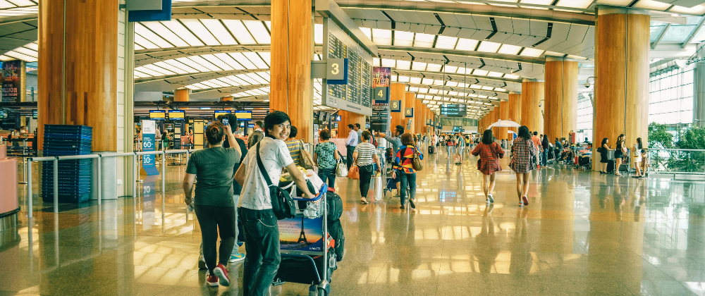 Travelers with luggage standing in an airport terminal near large windows overlooking the runway.